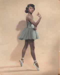 Joan Myers Brown in a light green costume posing on pointe in front of a brown background