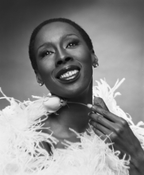 Black and white portrait photo of Judith Jamison smiling, posing in a feather costume